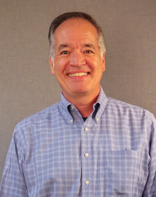 A professional headshot of Jef Fugita, a smiling man with graying hair wearing a suit against a solid black background.