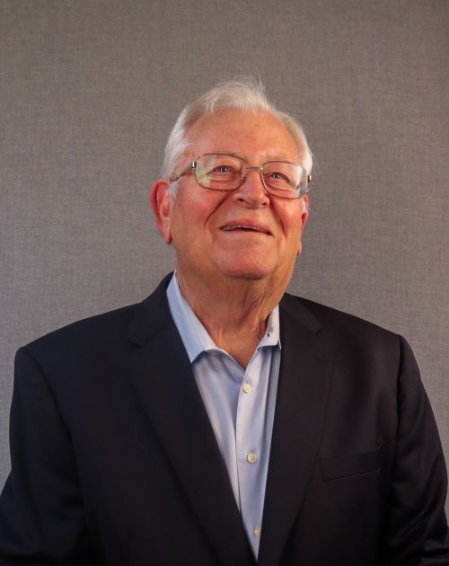 A headshot of Dennis Edmonds, an older man with white hair and glasses.