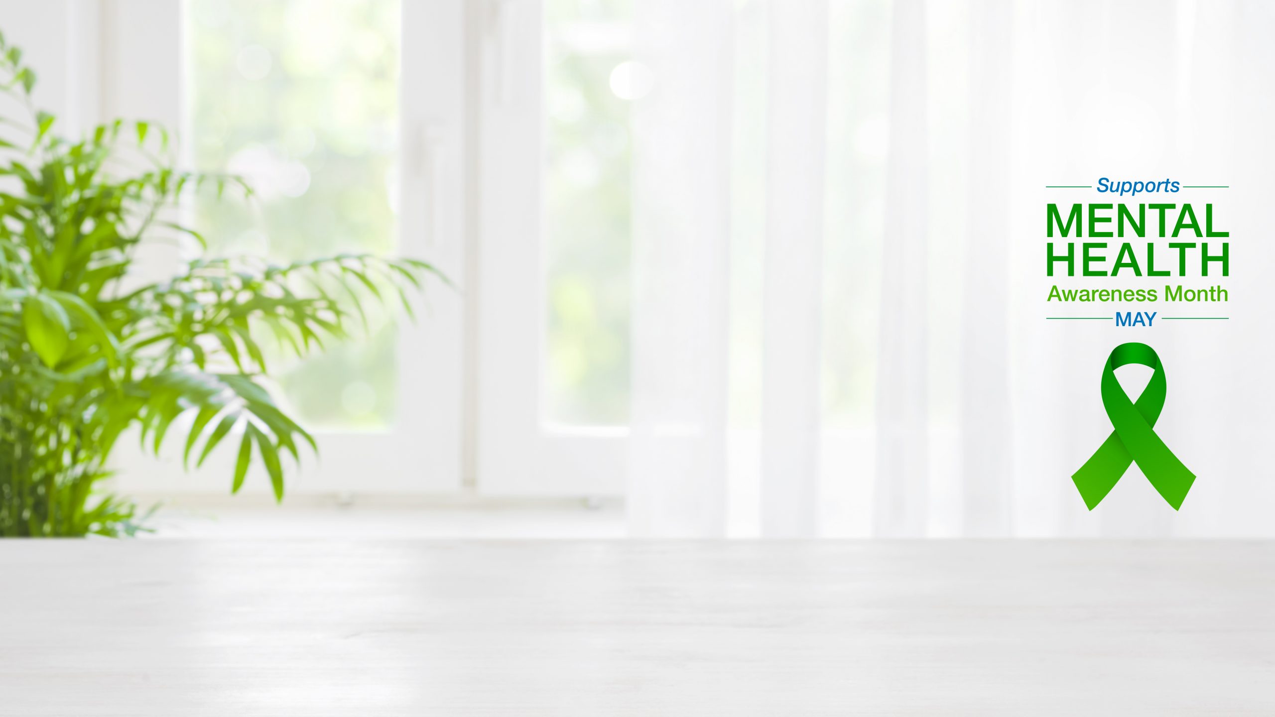 A digital background for virtual meetings. The background image is a soft-focus photo of a bright room with a plant and a window. On the right side is a graphic that reads, "Supports Mental Health Awareness Month - MAY -" above a green awareness ribbon.