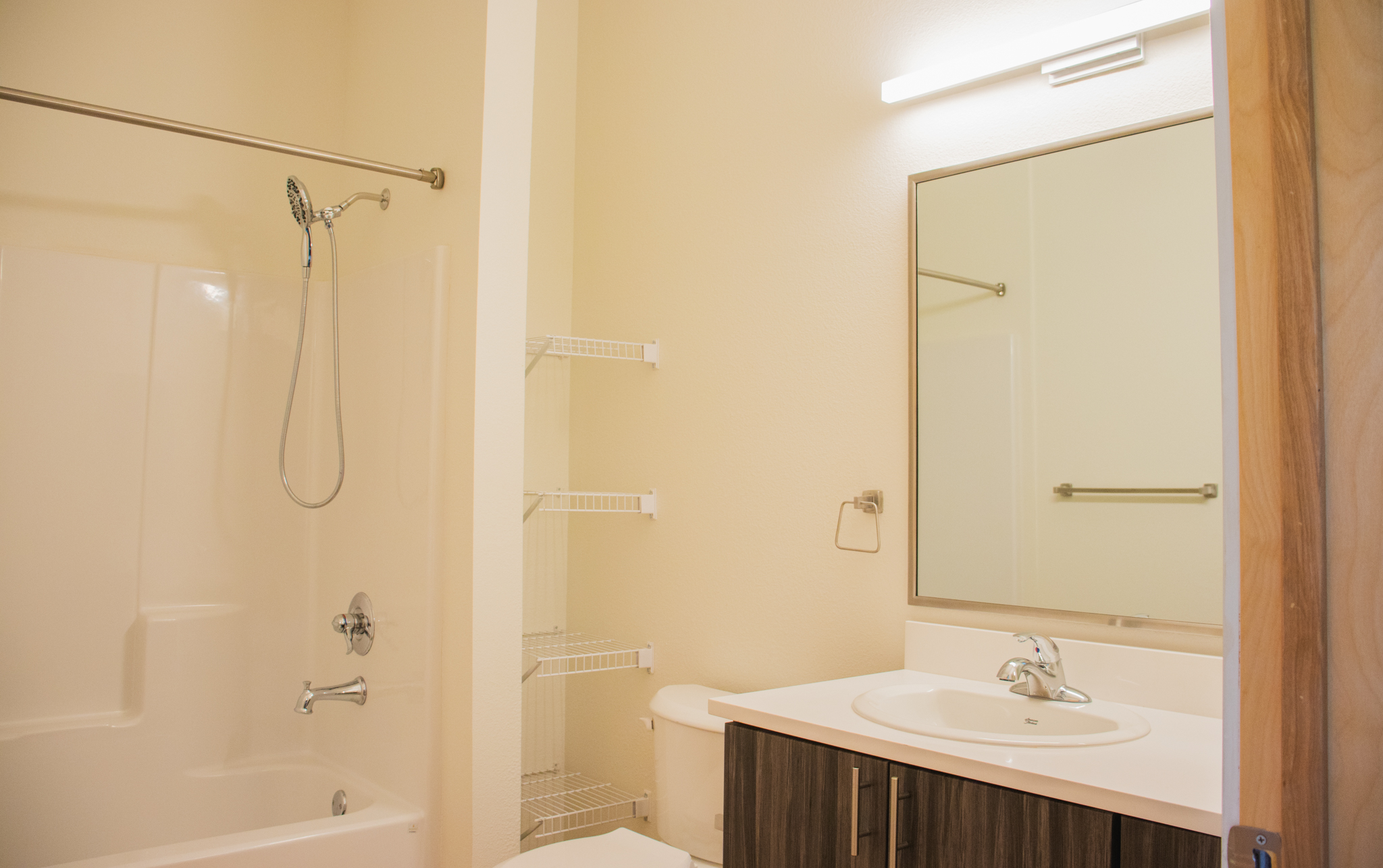 The clean, modern bathroom of a Solid Ground apartment. It includes a white shower and tub combination, a toilet, and a vanity with a dark wood-grain cabinet and a large mirror.
