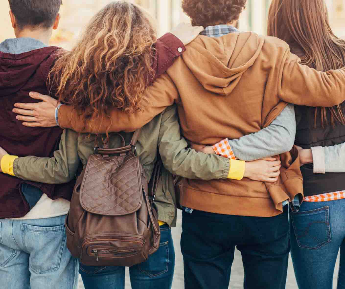 Von hinten betrachtet stehen vier Freunde Seite an Seite und haben ihre Arme um die Schultern und Taillen des anderen geschlungen, was Freundschaft und Unterstützung symbolisiert.