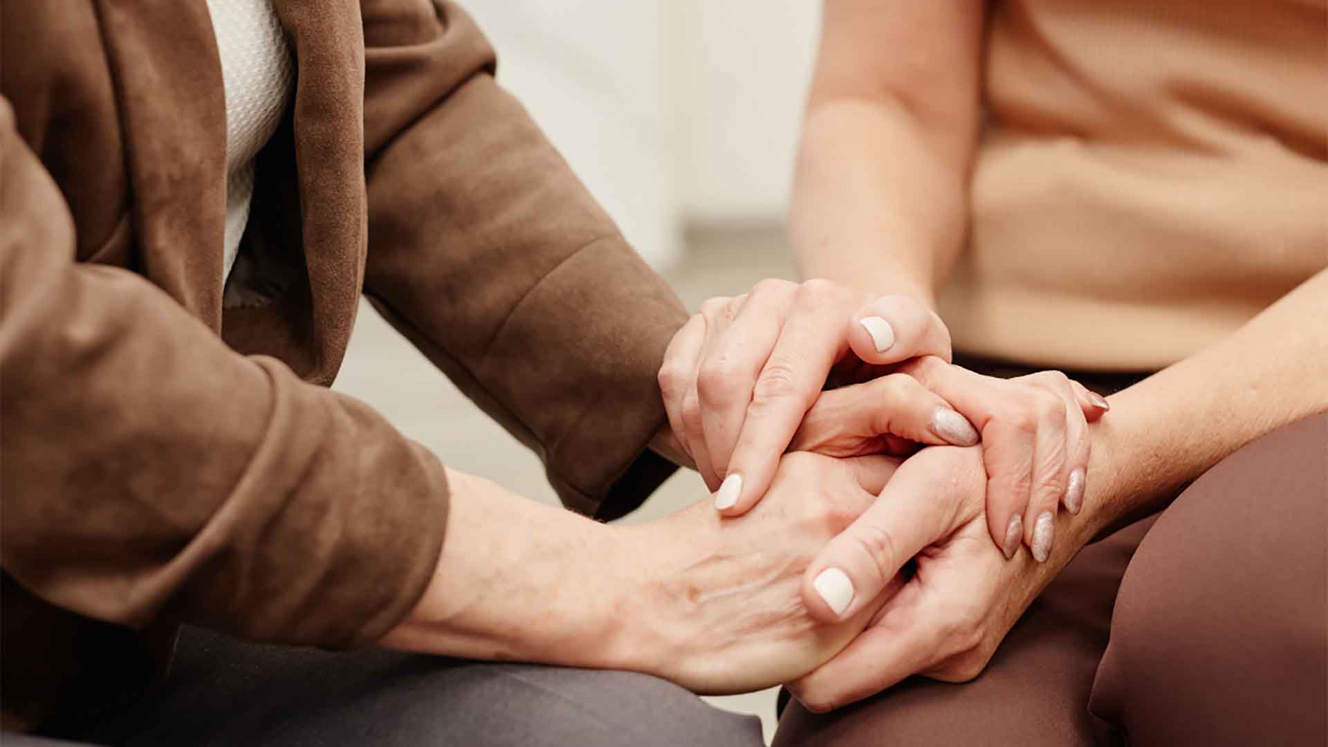 A close-up shot of a younger woman's hands gently holding the hands of an older woman in a gesture of comfort and support